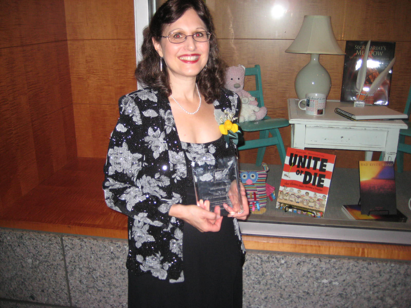 Jacqueline holding her engraved crystal book in front of a display with Unite or Die: How Thirteen States Became a Nation